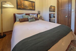 A neatly made bed with a green blanket, a wooden floor lamp, and a painting above the bed. - Walk to Square and U of A Historic Home (Fayetteville)