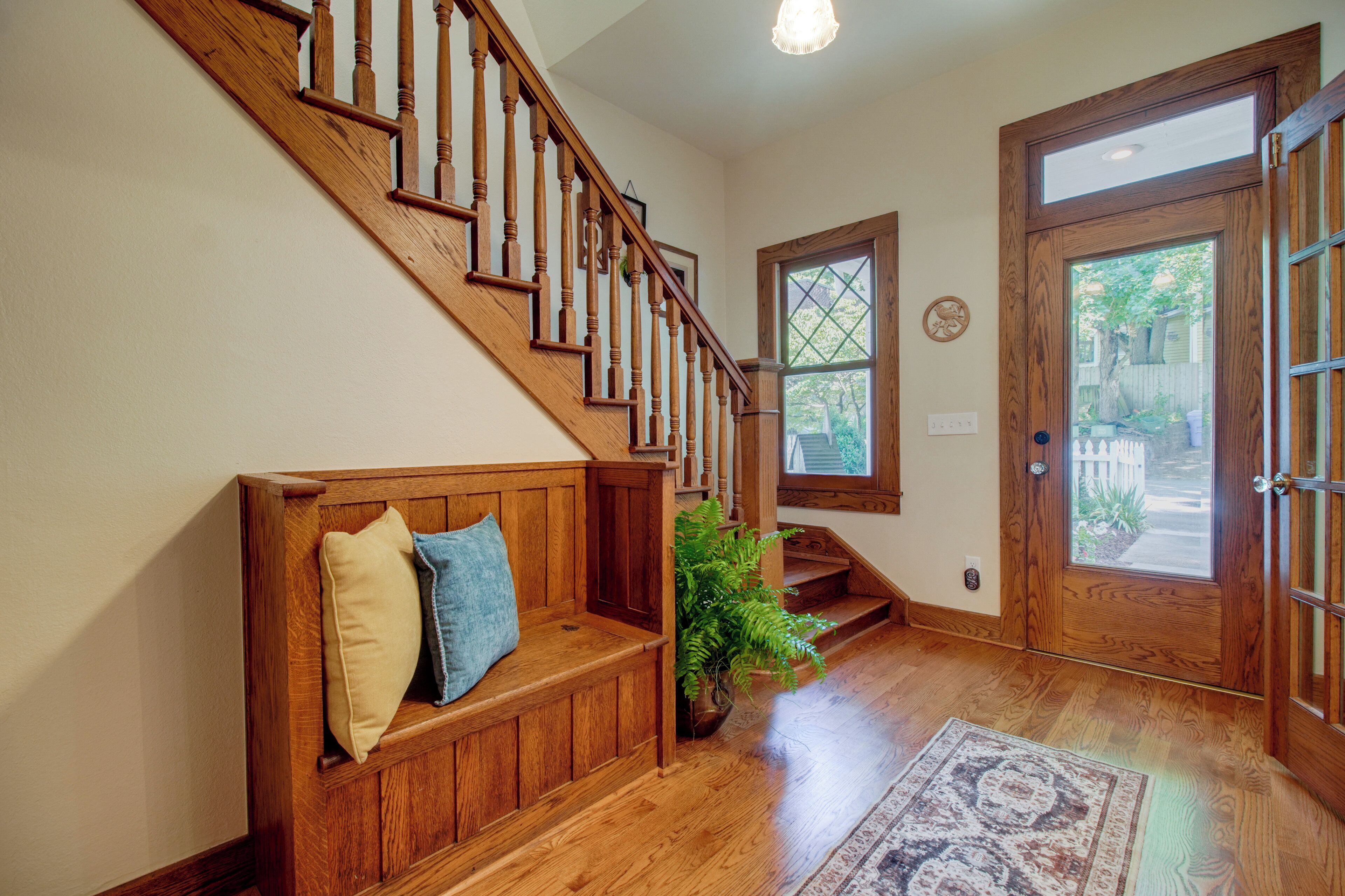 A wooden staircase with a bench at the bottom, a door with glass panels, and a window with a geometric design.