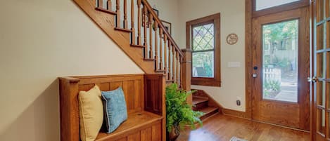 A wooden staircase with a bench at the bottom, a door with glass panels, and a window with a geometric design.