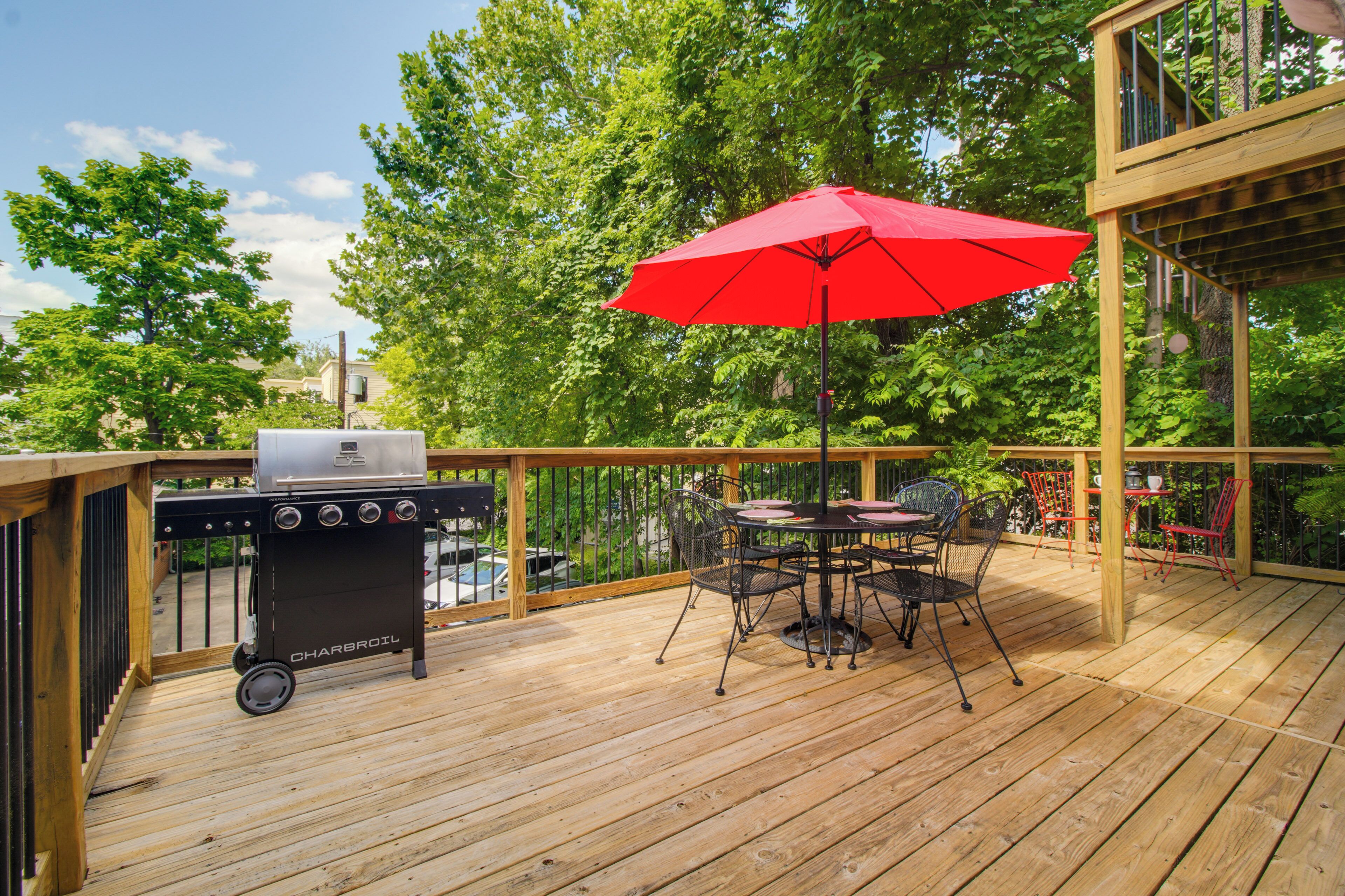 A wooden deck with a grill, a table with chairs, and a red umbrella.