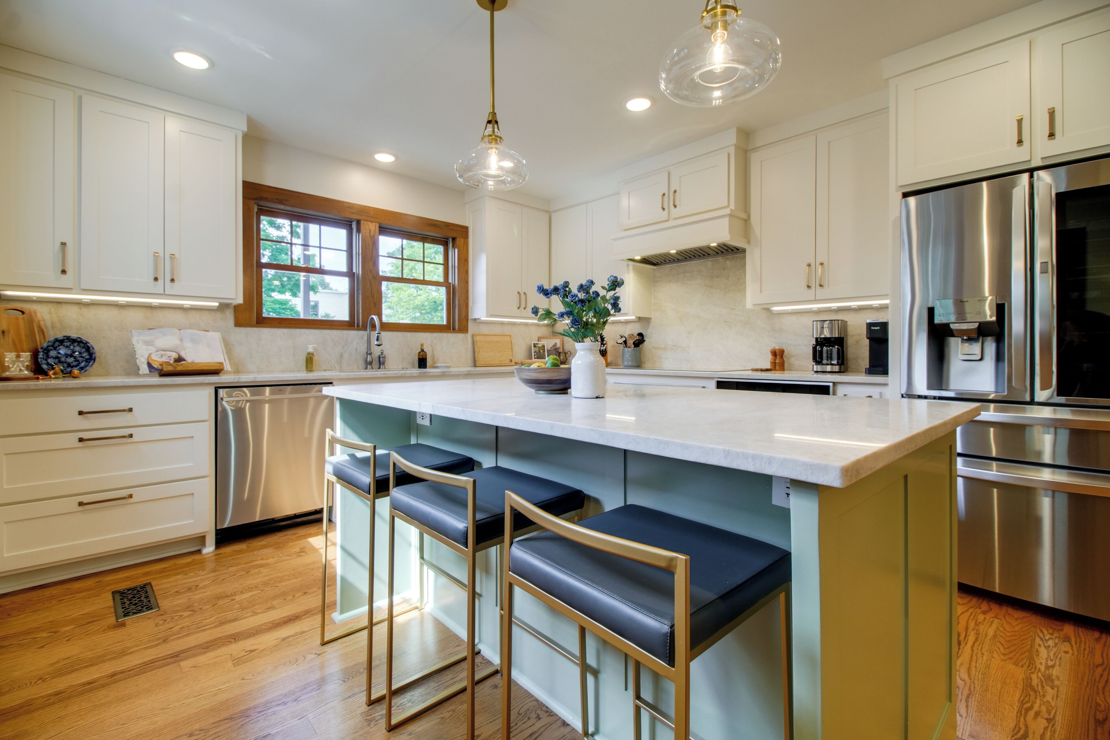A kitchen with white cabinets, stainless steel appliances, and a large island with bar stools.