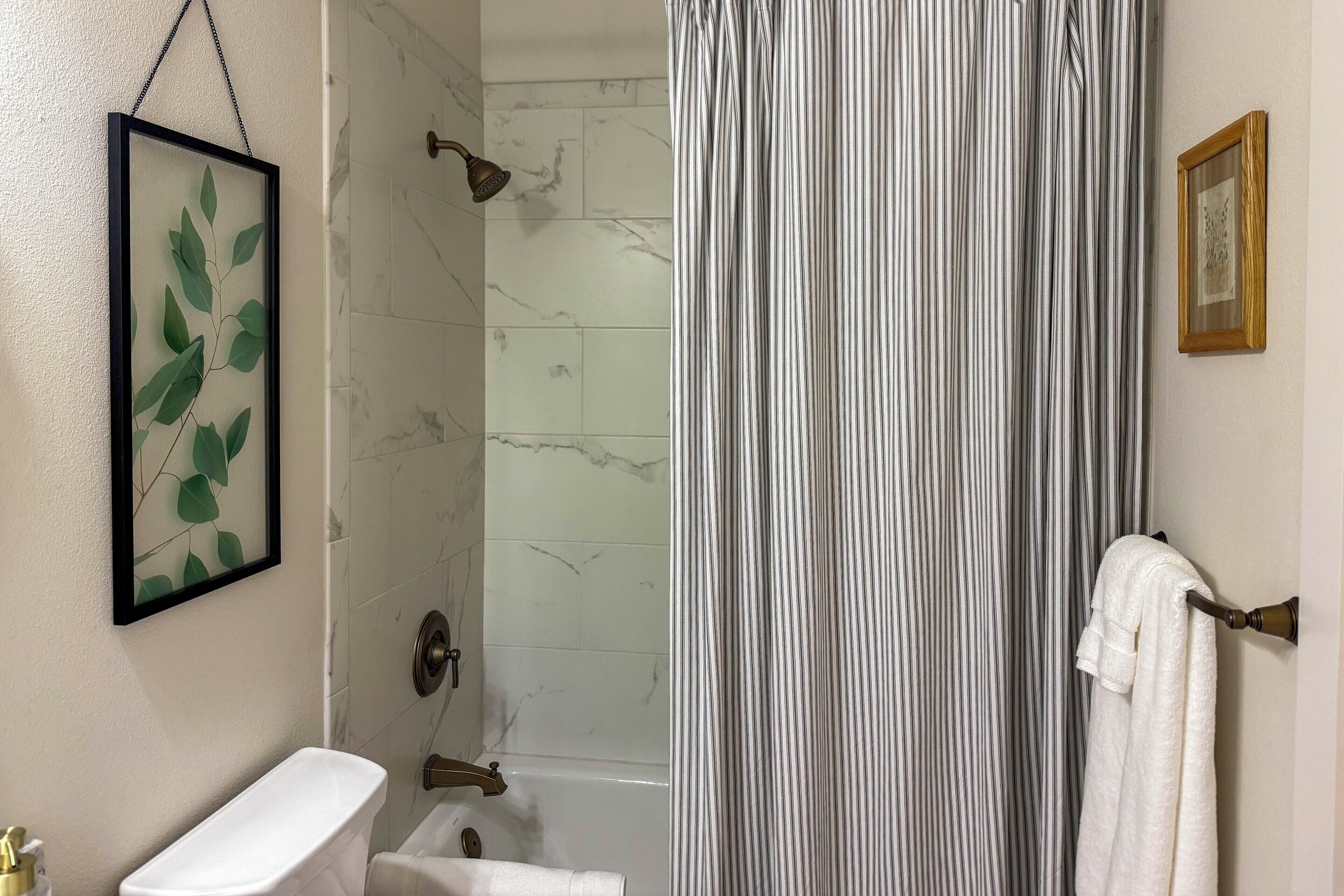 A bathroom with a toilet, a shower with a curtain, and a framed picture on the wall.