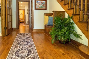 Un pasillo con piso de madera, un tapete con diseño, un banco con cojines y una escalera con barandillas de madera.