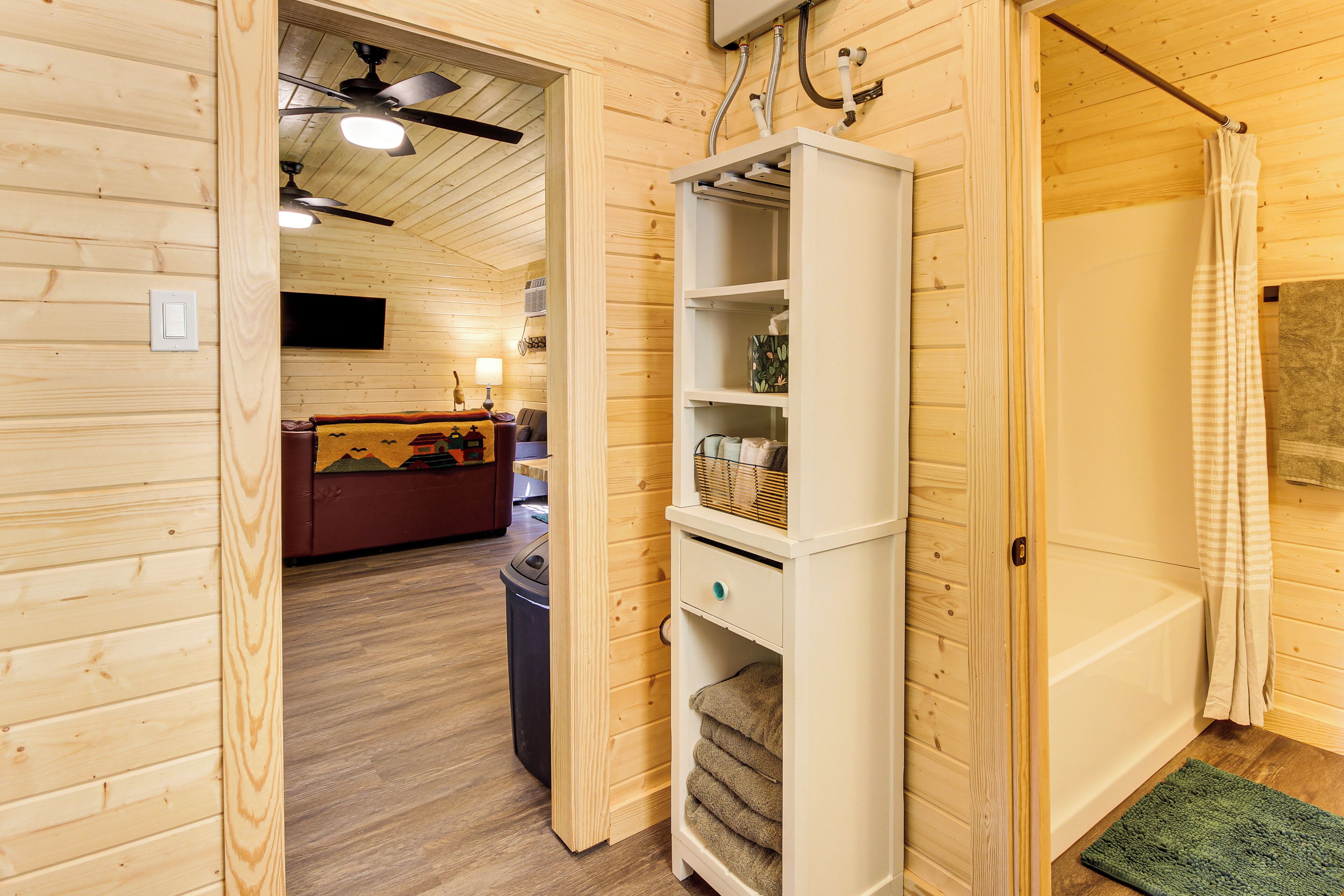 A wooden interior with a white shelving unit, a ceiling fan, and a visible bathroom area.