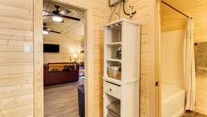 A wooden interior with a white shelving unit, a ceiling fan, and a visible bathroom area.
