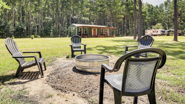 A cabin with a porch, a fire pit, and two Adirondack chairs.