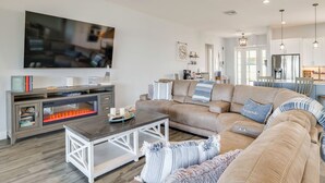 A modern living room with a large flat-screen TV, a sectional sofa, a coffee table, and a fireplace. - Boat Dock & Poolside Fun! Twin Houses on Lake Clay (Lake Placid)