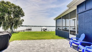 A patio with a view of a lake, a covered area with a table and chairs, and a grill. - Boat Dock & Poolside Fun! Twin Houses on Lake Clay (Lake Placid)