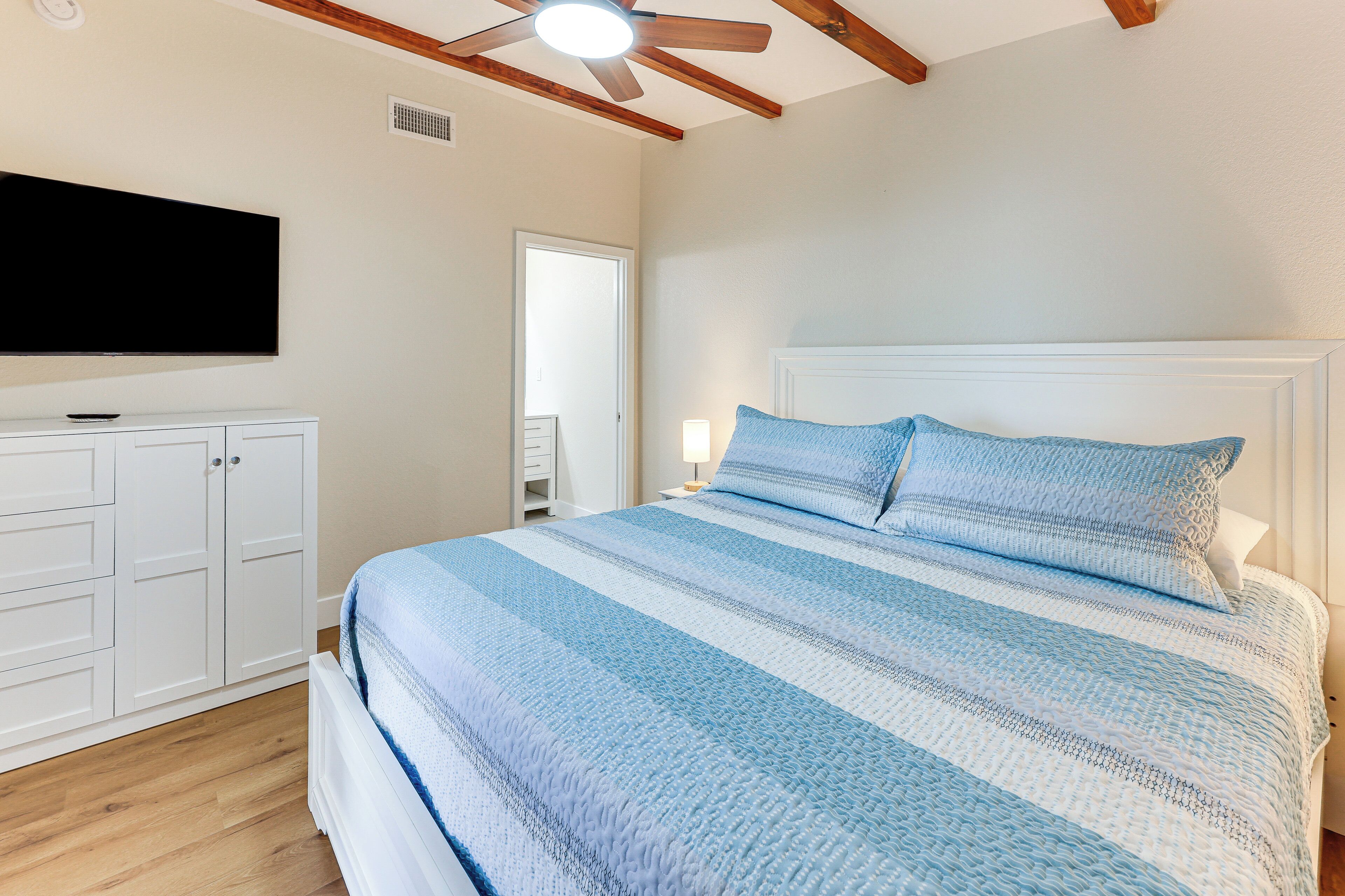 A bedroom with a bed, white wardrobe, ceiling fan, and a TV mounted on the wall.
