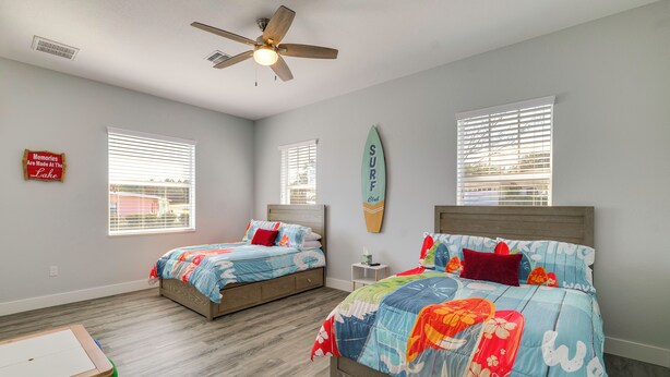 A bedroom with two beds, a ceiling fan, and a surfboard decoration. - Boat Dock & Poolside Fun! Twin Houses on Lake Clay (Lake Placid)