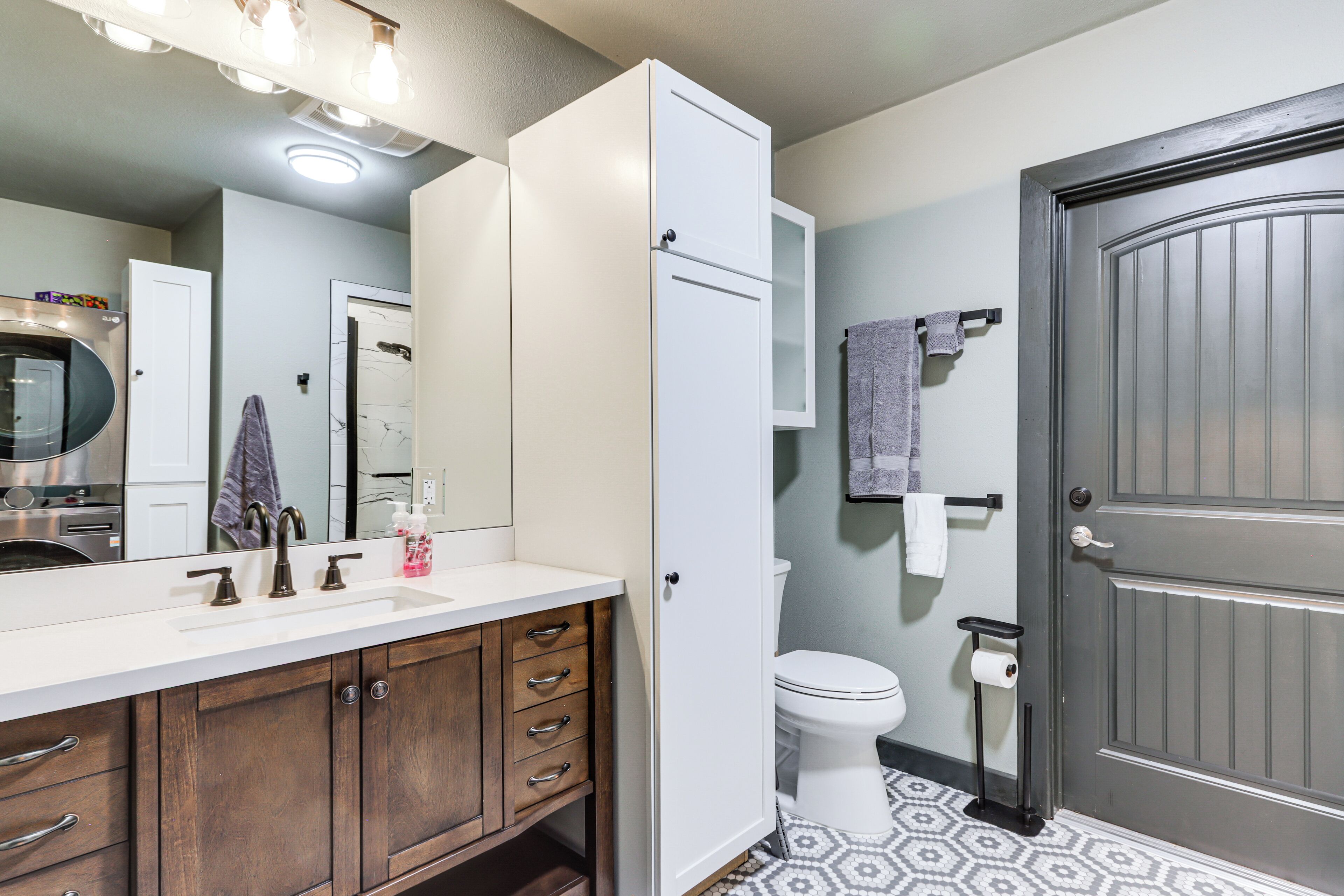 A bathroom with a white sink, wooden cabinets, a toilet, and a door.