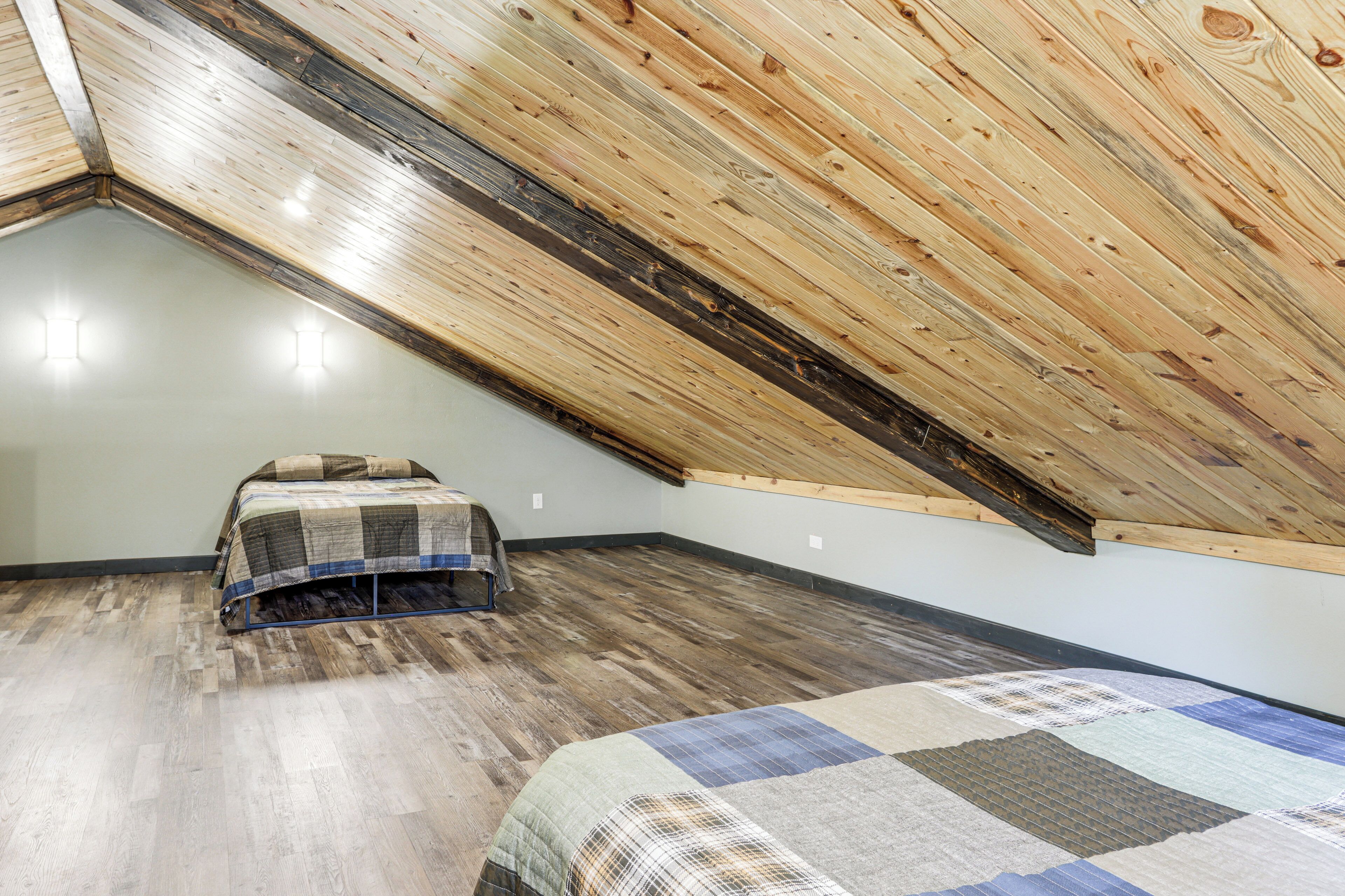 A room with a sloped ceiling, a bed with a quilt, and a small table.