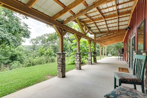 A covered outdoor area with stone pillars, a concrete floor, and a view of the surrounding greenery.