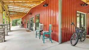 Uma área externa coberta com um edifício vermelho, duas cadeiras, uma mesa e uma bicicleta.