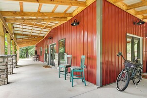 Un espacio exterior cubierto con un edificio rojo, dos sillas, una mesa y una bicicleta.