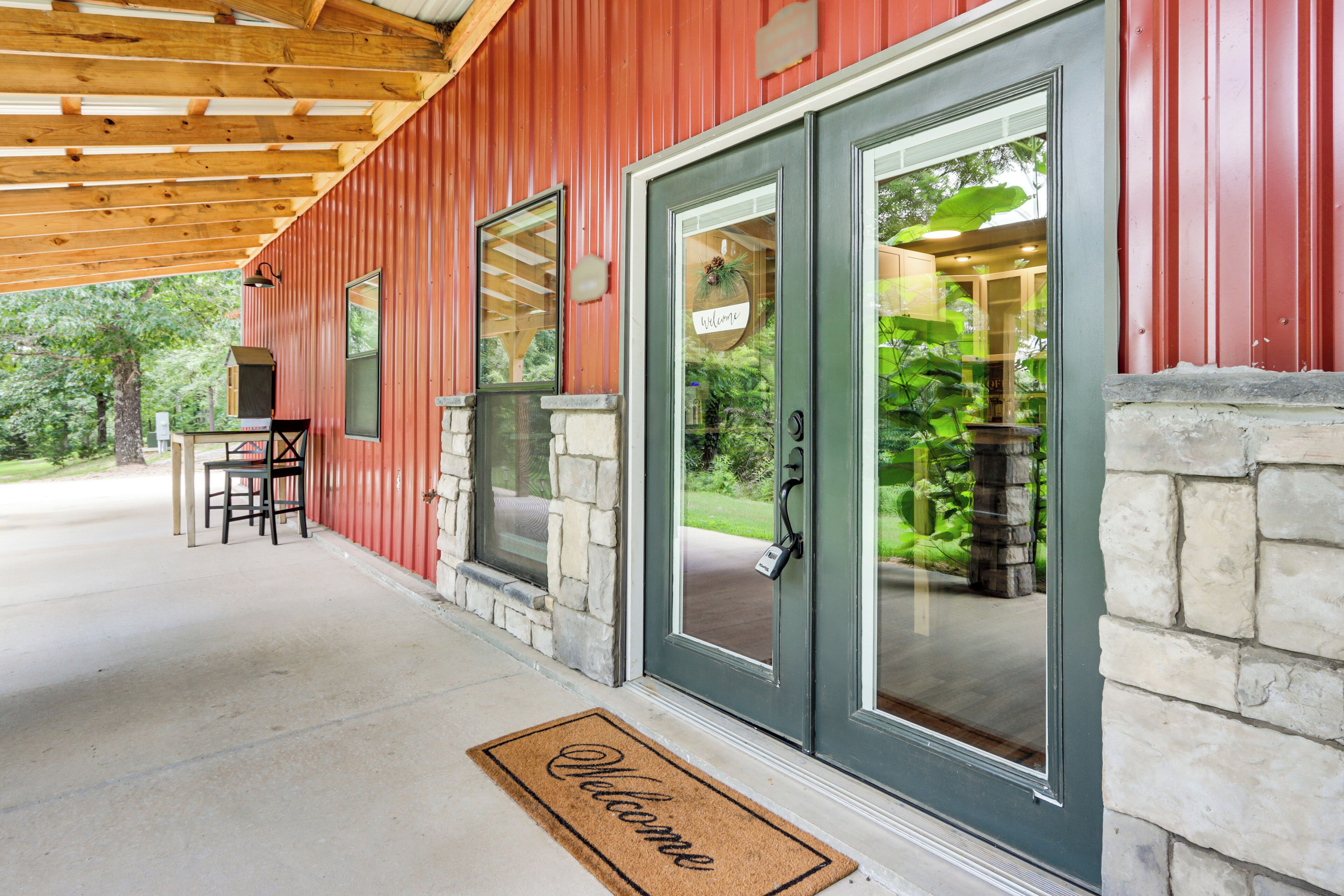 A red building with a stone foundation, a welcome mat, and a covered porch with chairs.