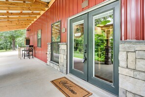 A red building with a stone foundation, a welcome mat, and a covered porch with chairs.