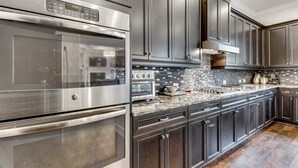 Une cuisine moderne dotée d’appareils électroménagers en acier inoxydable, de meubles de rangement aux couleurs sombres et d’un dosseret carrelé.