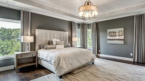 Une chambre à coucher avec un grand lit, une table de chevet, un lustre et une fenêtre avec des rideaux.