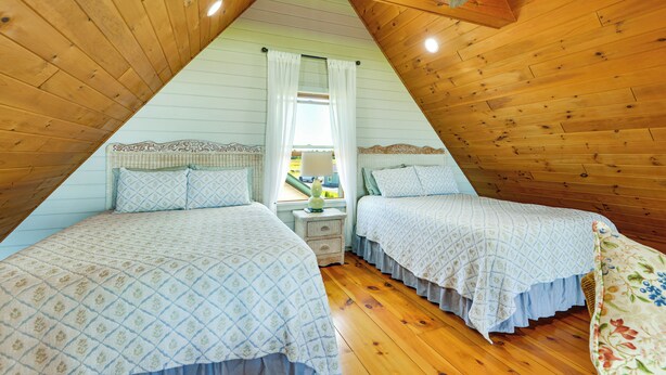 A bedroom with two beds, wooden walls, a sloped ceiling, and a window with curtains. - Fisherman's Retreat on Lake Ontario, Near Marina (Cape Vincent)