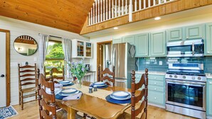 A wooden dining table set with plates, surrounded by chairs, in a kitchen with light green cabinets and stainless steel appliances. - Fisherman's Retreat on Lake Ontario, Near Marina (Cape Vincent)
