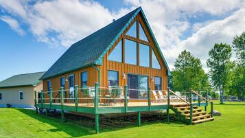 A wooden cabin with a large deck, multiple windows, and a steeply pitched roof.