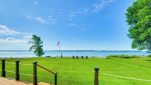 A deck with a view of a grassy area, a flag, and a body of water. - Fisherman's Retreat on Lake Ontario, Near Marina (Cape Vincent)
