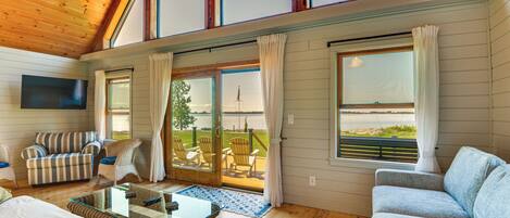 A spacious room with a wooden ceiling, large windows, a flat-screen TV, and a view of the outdoors.