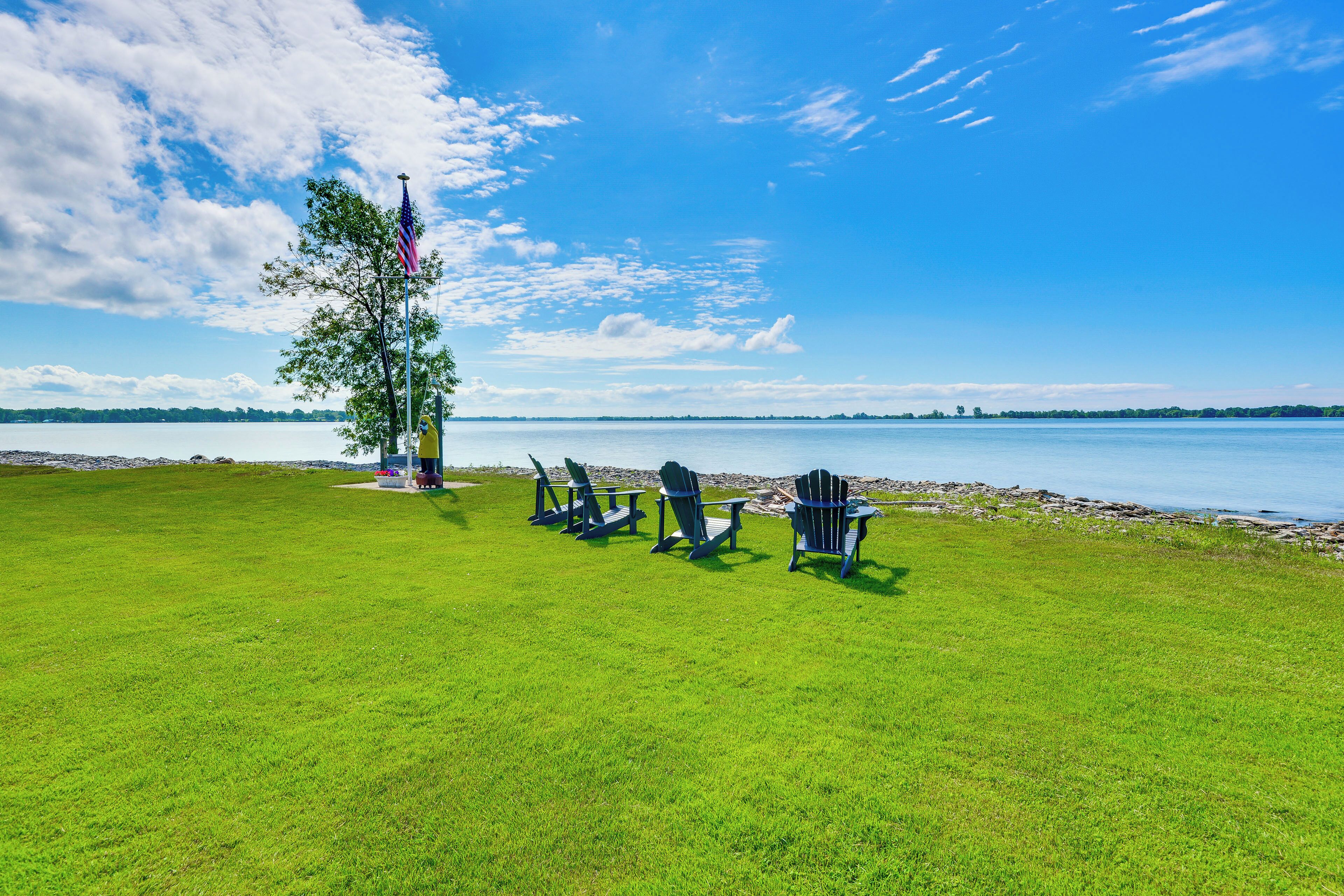 A grassy area with Adirondack chairs and a flagpole with an American flag.