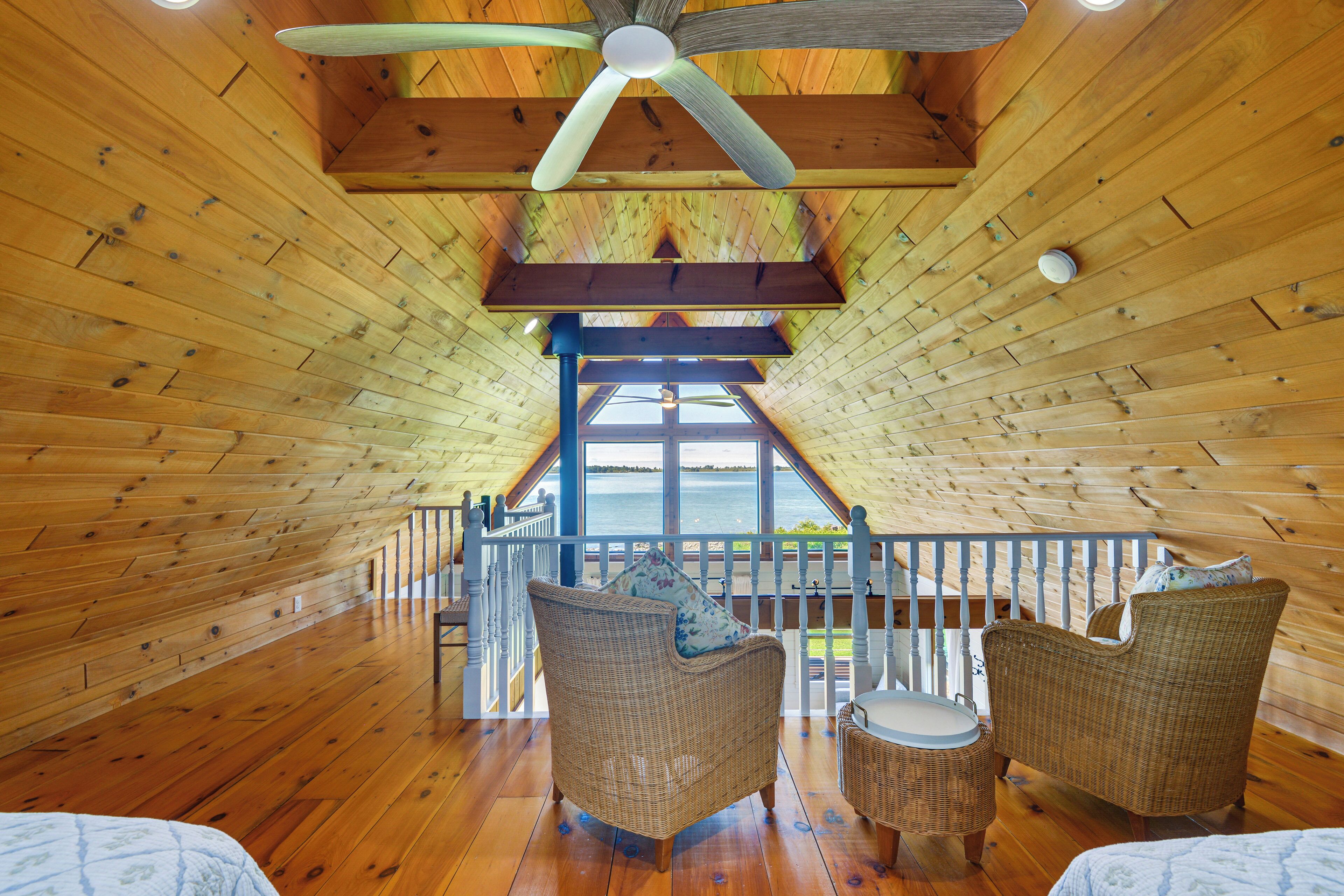 A wooden interior with a high ceiling, a ceiling fan, and a view of the outdoors through large windows.