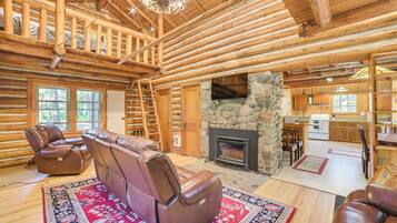 A log cabin interior with a fireplace, leather seating, and a stone wall.