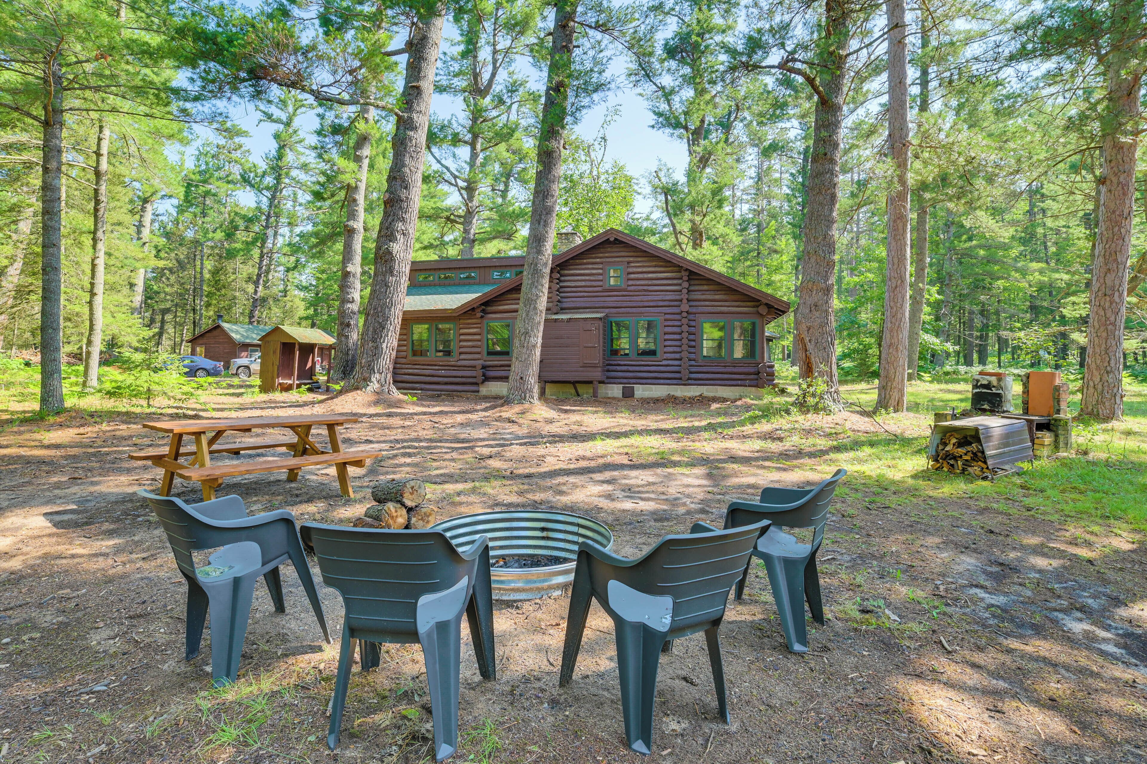 A rustic cabin with a picnic table and plastic chairs in a forest setting.