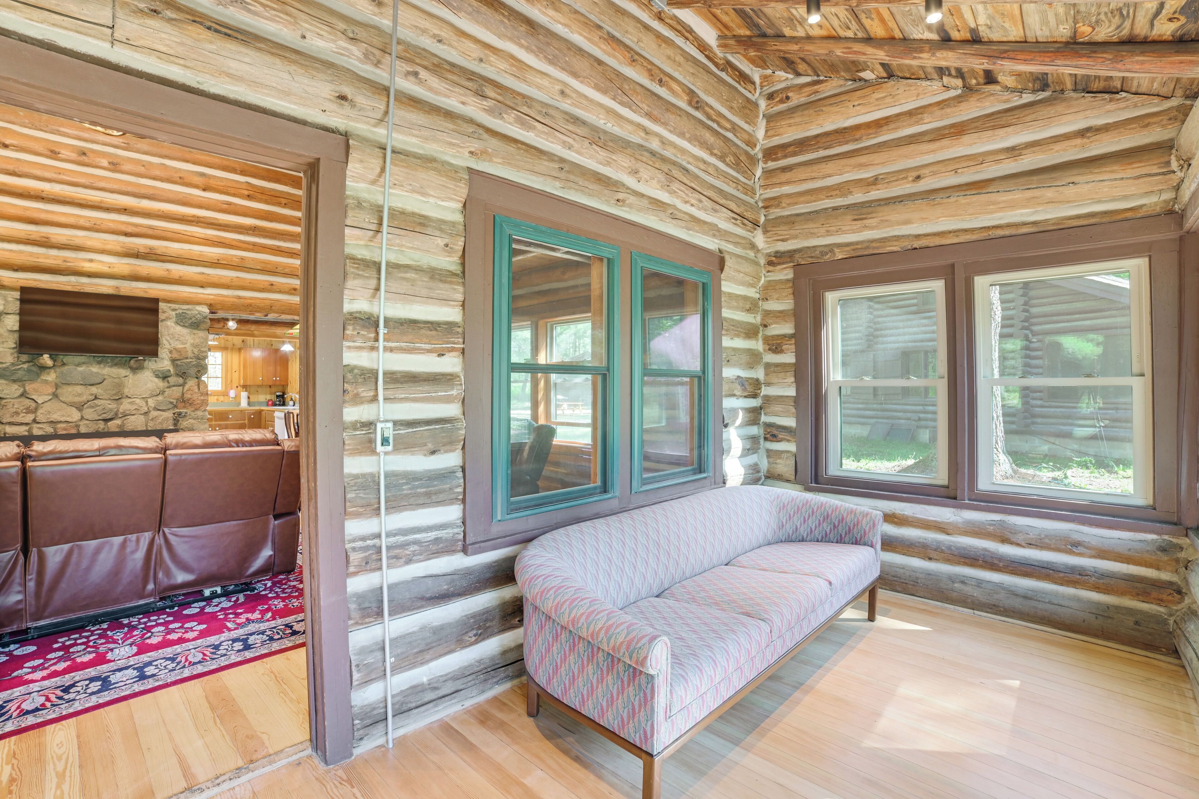 A log cabin interior with a sofa, a dining area, and large windows.