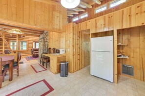 Interior de una cabaña de madera con comedor, cocina y pared de piedra.