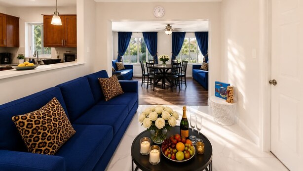 A modern living room with a blue sofa, a dining area with blue curtains, and a kitchen with wooden cabinets.