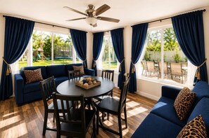 A room with a round table, blue sofas, and a ceiling fan.