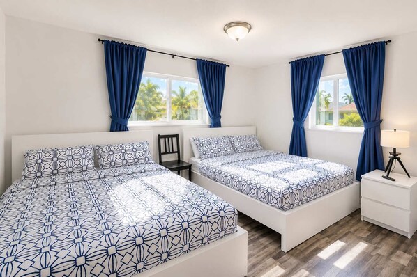A bedroom with two beds, a nightstand, a chair, and a window with curtains.