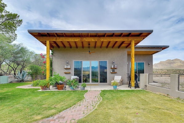 Una casa moderna con un porche cubierto, puertas correderas de vidrio grandes y un jardín ajardinado.