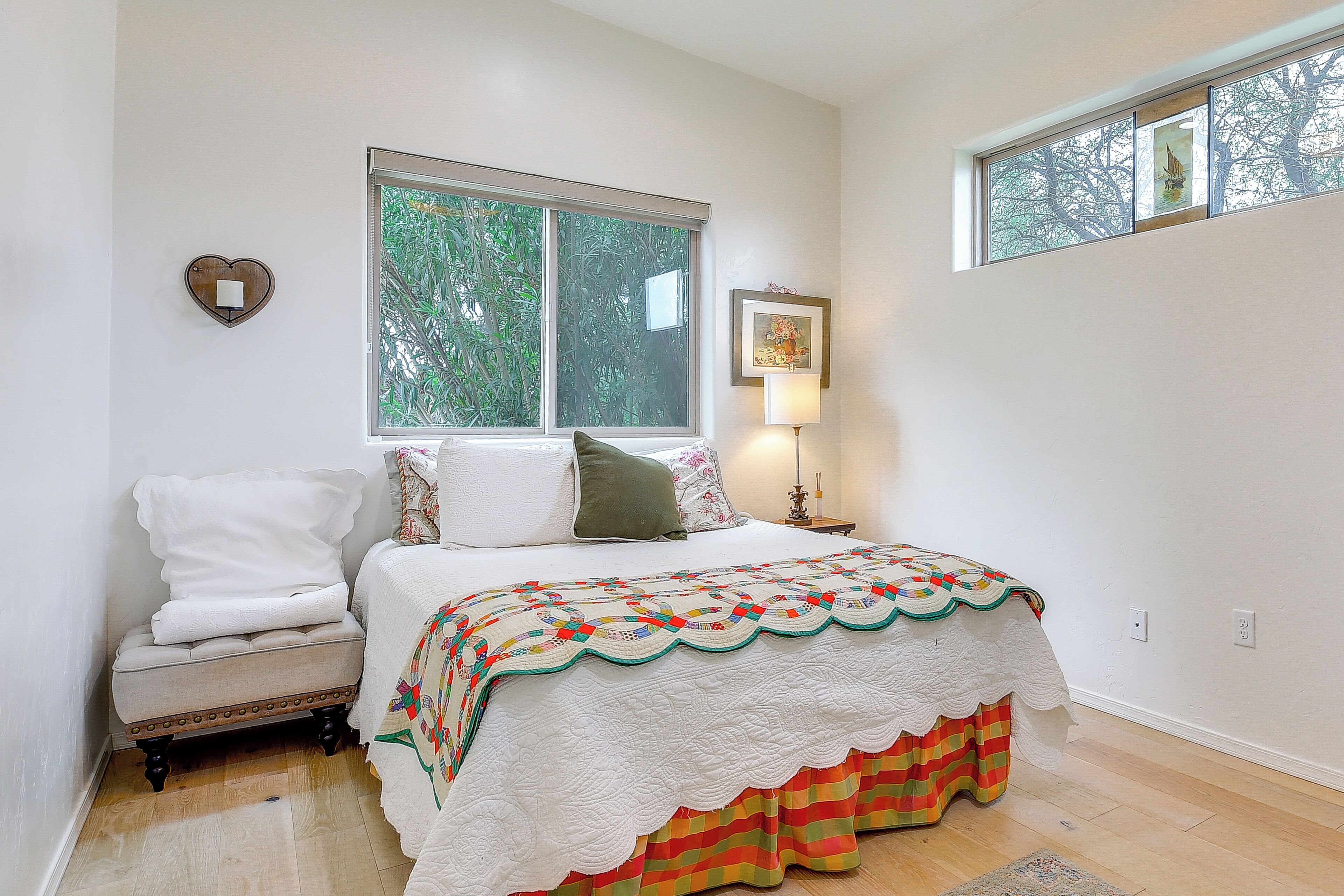 A bedroom with a bed, a nightstand, a window, and a heart-shaped wall decoration.