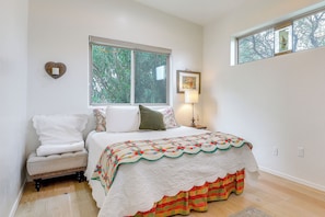 A bedroom with a bed, a nightstand, a window, and a heart-shaped wall decoration.