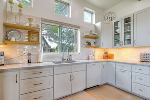 A modern kitchen with white cabinetry, a large window, and a view of trees outside.