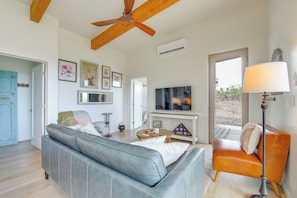 A living room with a sofa, a television, a ceiling fan, and a door leading outside.