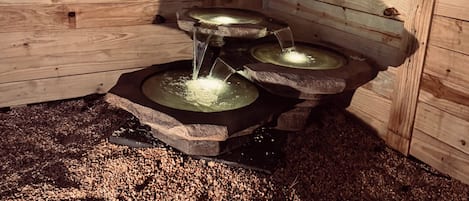 Una estructura de madera con una fuente de agua formada por tres estanques circulares.