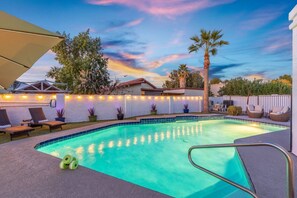 A swimming pool with lounge chairs and potted plants, surrounded by a white fence and a sunset sky. - Walk to Spring Training Heated Pool Sleeps 12 (Mesa)