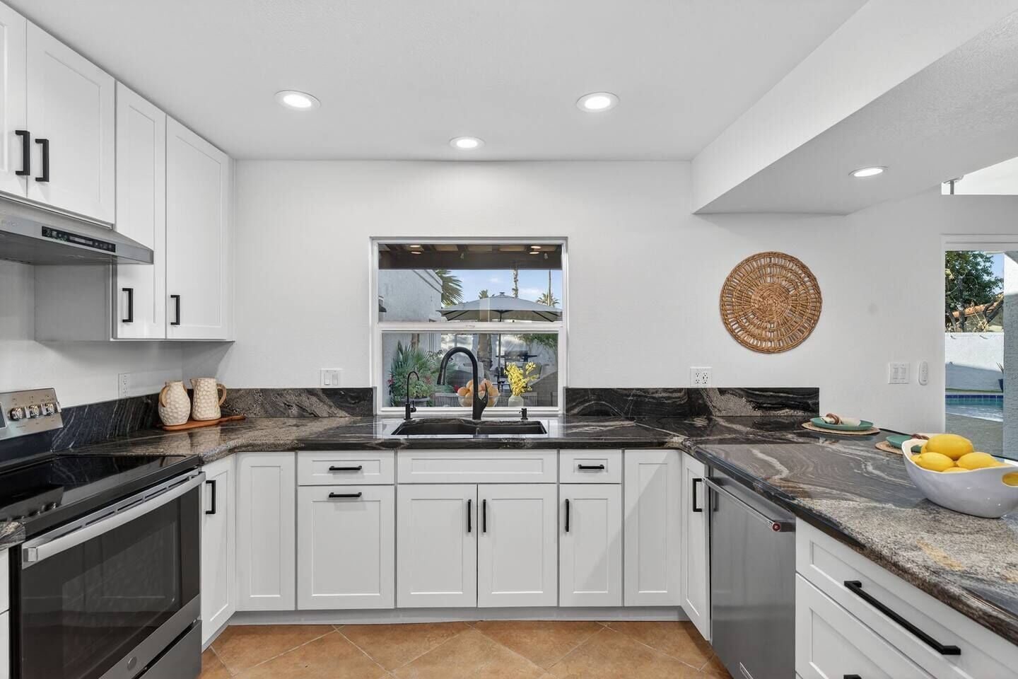 A modern kitchen with white cabinets, a black countertop, and a window overlooking a residential area.