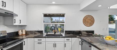 A modern kitchen with white cabinets, a black countertop, and a window overlooking a residential area.