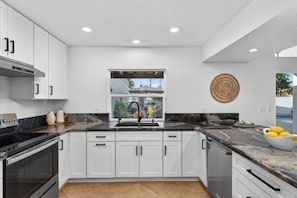 Una cocina moderna con armarios blancos, encimera negra y ventana con vistas a una zona residencial.