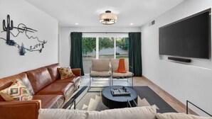 Ein modernes Wohnzimmer mit einem Ledersofa, zwei Sesseln, einem Couchtisch und einem flachbildfernseher an der Wand.