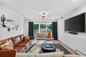 A modern living room with a leather sofa, two armchairs, a coffee table, and a flat-screen TV mounted on the wall. - Mesa Retreat Heated Pool Game Room Great For Families (Mesa)