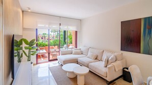 Uma sala de estar moderna com um sofá seccional, uma TV de tela plana, uma mesa de centro e uma janela grande com vista para o exterior.